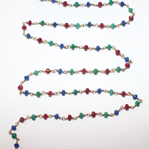May include: A gold chain with alternating red, blue, and green gemstone beads.