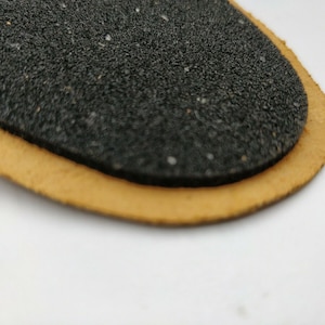 Op de afbeelding: Een close-up van een zwarte, getextureerde, ovale patch met een bruine leren rand.