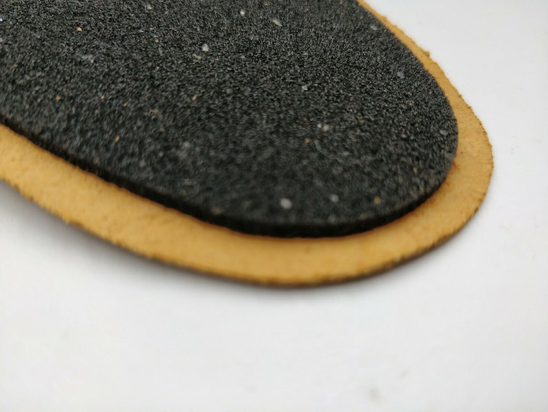 Op de afbeelding: Een close-up van een zwarte, getextureerde, ovale patch met een bruine leren rand.