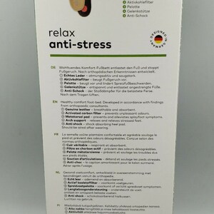 Op de afbeelding: Een witte doos met een paar bruine en zwarte inlegzolen. Op de voorkant van de doos staat "solos relax anti-stress". De inlegzolen zijn gemaakt van echt leer en hebben een actieve koolstoffilter, een spreidvoetkussen, een voetboogondersteuning en een anti-shock hielkussen.