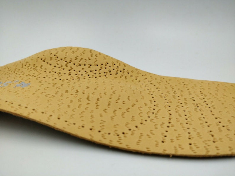 Op de afbeelding: Een beige leren inlegzool met een patroon van kleine gaatjes. De inlegzool is gebogen om de vorm van een voet te passen.