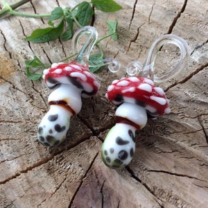 May include: Two glass mushroom earrings with red and white caps, black and white stems, and clear glass hooks.