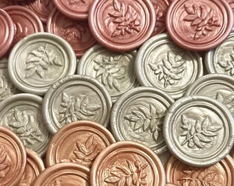 May include: A collection of round, metallic wax seals with a leaf design. The seals are in two colors: rose gold and silver.