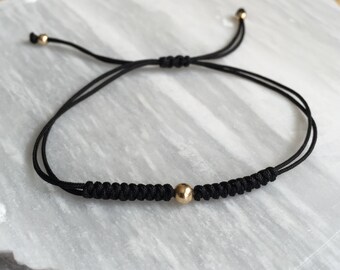 May include: A black string bracelet with a single gold bead in the center.