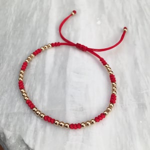 Puede incluir: Un brazalete de cuerda roja con cuentas doradas. El brazalete es ajustable y se puede llevar en la muñeca o en el tobillo.