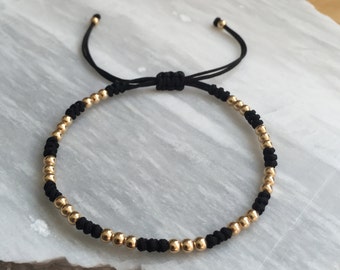 May include: A black string bracelet with gold beads. The bracelet is adjustable with a sliding knot.