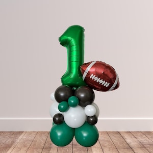 May include: Green number one balloon with a brown and white football balloon, surrounded by green, black, and white balloons.