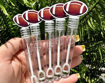 Pode incluir: Uma mão segura cinco varinhas de bolhas transparentes encimadas por adesivos em forma de bola de futebol. As bolas de futebol são marrons com listras brancas. As varinhas têm varinhas de bolhas brancas e tubos de plástico transparentes.