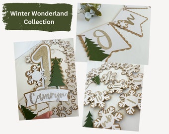 May include: A collection of winter-themed party decorations. Includes a cake topper with a gold glitter number one, a banner with the word "one", and a garland of snowflake-shaped numbers. The decorations are white, gold, and green.