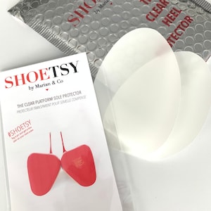 May include: A package containing clear heel protectors for shoes. The package is labeled "SHOETSY by Marian & Co. The Clear Heel Protector". The package also includes a pair of red shoe heels.