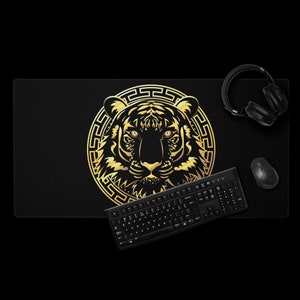 Könnte beinhalten: Schwarzes rechteckiges Mauspad mit einem goldenen Tigerdesign. Der Tiger ist zentriert und von einem dekorativen Rahmen umgeben. Eine schwarze Tastatur, Maus und Kopfhörer sind ebenfalls zu sehen.