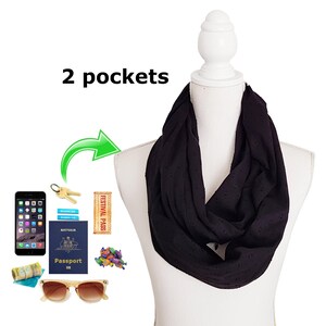 Pode incluir: Cachecol infinito preto com um padrão de bolinhas, exibido em um manequim branco. O cachecol tem dois bolsos e é mostrado com acessórios de viagem, como passaporte, óculos de sol e smartphone. O texto "2 pockets" é visível.