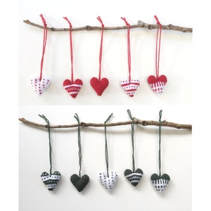 May include: Handmade heart-shaped decorations in red, white, and green, suspended from twigs. The ornaments display knitted patterns and solid colours, ideal for Valentine's Day or other celebrations. Each heart is hung by a matching string.