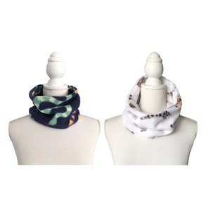 May include: Two fleece neck warmers on mannequins. One is navy blue with a green snake print and the other is white with a brown animal print.