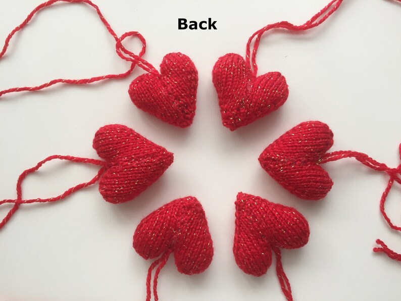 May include: Six red knitted heart ornaments with gold flecks are arranged in a circle. Each heart has a red string attached for hanging. The word "Back" is visible in the image. These ornaments are suitable for Valentine's Day or other celebrations.