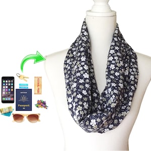 May include: A navy blue infinity scarf with a white floral pattern is displayed on a mannequin. The scarf is made of a soft fabric and is designed to be worn looped around the neck. Accessories such as a phone, passport, keys, and sunglasses are also shown.