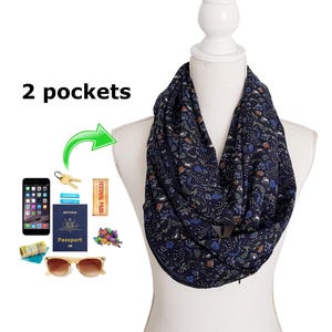 May include: Navy blue infinity scarf with a floral pattern, displayed on a mannequin. The scarf has two pockets and is accessorized with a phone, keys, sunglasses, a passport, and a festival pass.