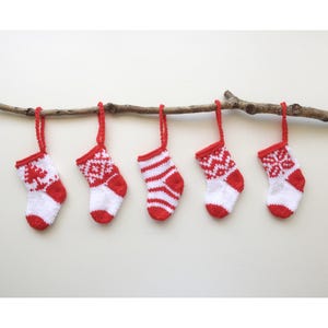 以下が含まれることがあります： 枝にぶら下がっている、赤と白の小さなニットの靴下5つ。靴下は、雪片、ストライプ、クリスマスツリーなど、さまざまなパターンがあります。