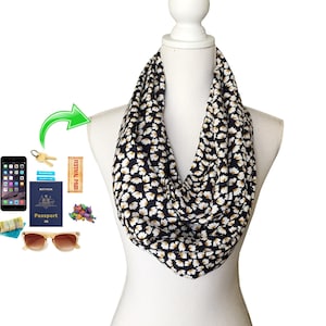 May include: An infinity scarf with a black background and a white floral pattern, displayed on a mannequin. The scarf is a loop design. Accessories such as a phone, passport, and sunglasses are shown.
