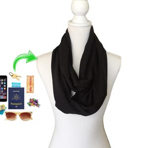 Könnte beinhalten: Schwarzer Infinity-Schal auf einer weißen Schaufensterpuppe. Der Schal besteht aus einem weichen, fließenden Stoff. Zubehör wie Smartphone, Schlüssel, Reisepass, Sonnenbrille und Festivalpass deuten auf Reisen hin.