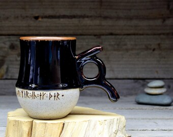 May include: A black and white ceramic mug with a unique handle. The mug has a black glaze and a white base with black runes that read "May your path be clear".