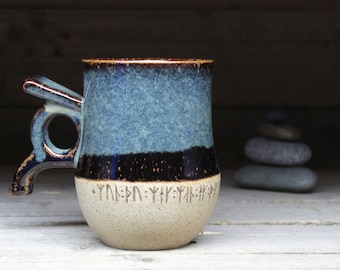 May include: A blue and brown ceramic mug with a unique handle and a band of runes around the bottom.