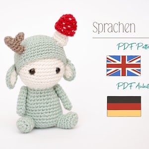 May include: A crocheted doll in a light green outfit with a mushroom hat and small antlers. The doll has a cream-colored face and large black eyes. The image also includes the text "Sprachen", "PDF Pattern", and "PDF Anleitung", along with the flags of the UK and Germany.