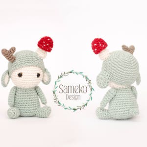 May include: Crocheted deer doll with a mushroom hat. The doll is light green with a cream-colored face and ears. It has brown antlers and a red and white mushroom on its head. The doll is sitting with its arms and legs outstretched.