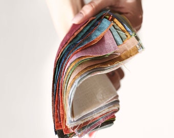 Puede incluir: Una mano sostiene un abanico de muestras de tela en varios colores. Las muestras incluyen tonos de rojo, verde, azul, amarillo y tonos neutros. La tela parece ser lino o un material similar, con una superficie ligeramente texturizada.