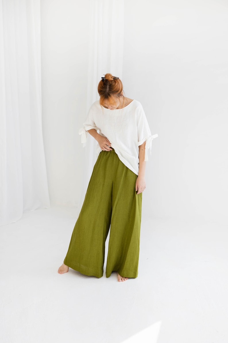 K&ouml;nnte beinhalten: Ein Outfit f&uuml;r Damen, bestehend aus einem wei&szlig;en Leinenoberteil mit Bindedetails an den &Auml;rmeln und einer olivgr&uuml;nen Hose mit weitem Bein. Das Outfit ist schlicht und elegant, perfekt f&uuml;r den Alltag. Die Hose hat eine lockere Passform.