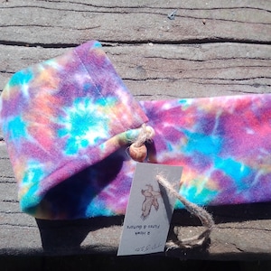 May include: A tie-dye fleece pouch with a drawstring closure and a small wooden bead. The pouch is tied with twine and has a tag that reads "The Home & Feathers & Goods".