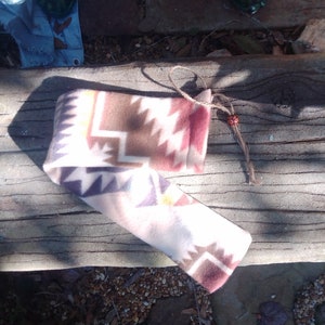 Könnte beinhalten: Eine kleine, rechteckige Tasche aus braunem, weißem, rotem und violettem gemustertem Fleece-Stoff. Die Tasche ist mit einer braunen Schnur und einer kleinen braunen Perle verschlossen.