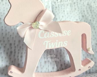 May include: Pink wooden rocking horse with a pink bow and rhinestones. The horse is personalized with the name "Cassee Twins" and the text "Gem's crafty gifts".