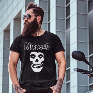 K&ouml;nnte beinhalten: Ein schwarzes T-Shirt mit einem wei&szlig;en Grafikdruck eines Sch&auml;dels und dem Text "Maroon 5" auf der Vorderseite.