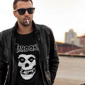 K&ouml;nnte beinhalten: Ein Mann tr&auml;gt eine schwarze Lederjacke &uuml;ber einem schwarzen T-Shirt mit einem wei&szlig;en Totenkopf-Motiv und dem Text "MAROON 5".