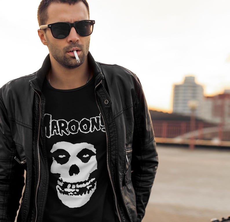 K&ouml;nnte beinhalten: Ein Mann tr&auml;gt eine schwarze Lederjacke &uuml;ber einem schwarzen T-Shirt mit einem wei&szlig;en Totenkopf-Motiv und dem Text "MAROON 5".