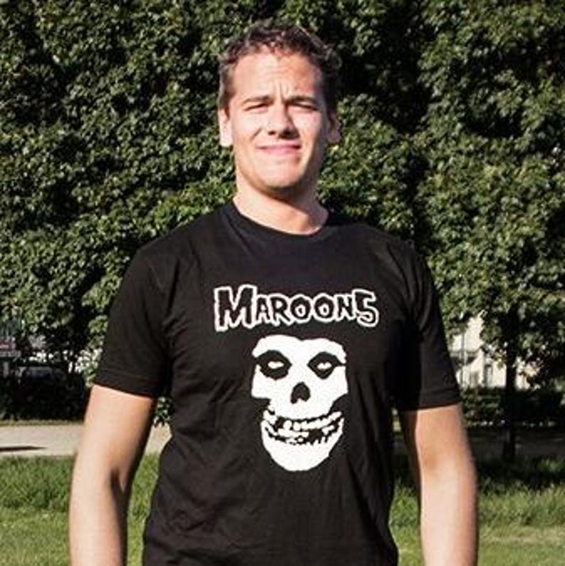 K&ouml;nnte beinhalten: Ein schwarzes T-Shirt mit einem wei&szlig;en Grafikdruck eines Sch&auml;dels mit dem Text "Maroon 5" dar&uuml;ber.