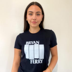 Könnte beinhalten: Ein schwarzes T-Shirt mit einem weißen Grafikdruck eines stilisierten Fausts mit dem Text "BRYAN FERRY" darüber und darunter.