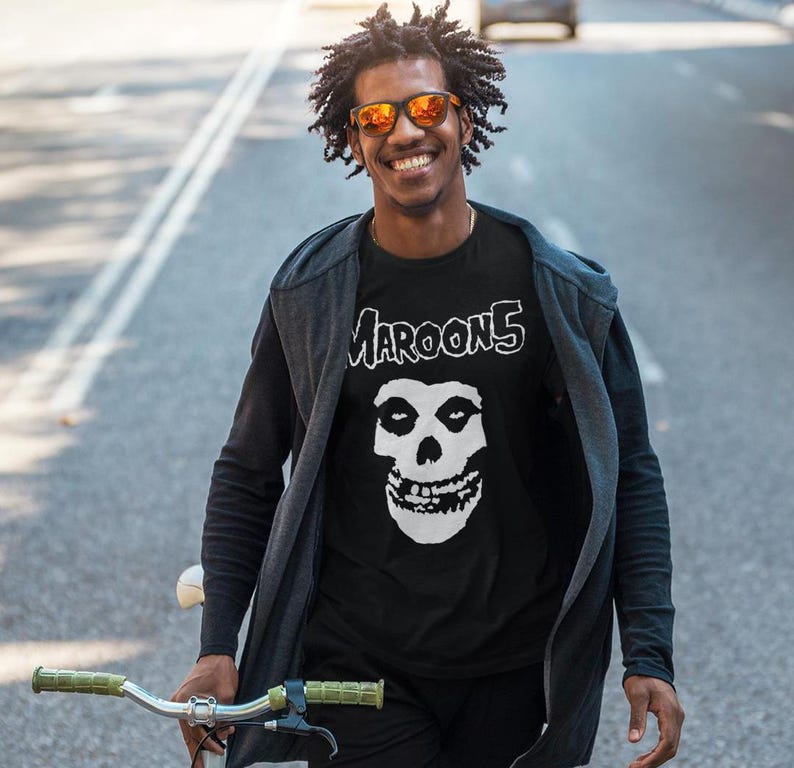 K&ouml;nnte beinhalten: Ein Mann tr&auml;gt ein schwarzes T-Shirt mit einem wei&szlig;en Totenkopf-Motiv und dem aufgedruckten Text "MAROON 5". Er tr&auml;gt eine schwarze Jacke und eine Sonnenbrille.