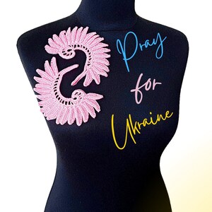 May include: A pink crocheted lace design on a black mannequin with the text "Pray for Ukraine" in blue, pink, and yellow.