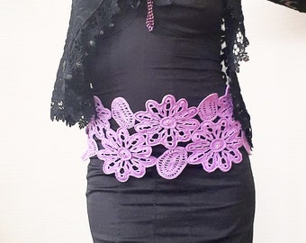 May include: A black lace jacket with a purple flower lace belt. The jacket has a deep V-neckline and long sleeves. The belt is tied at the waist and has a floral design.