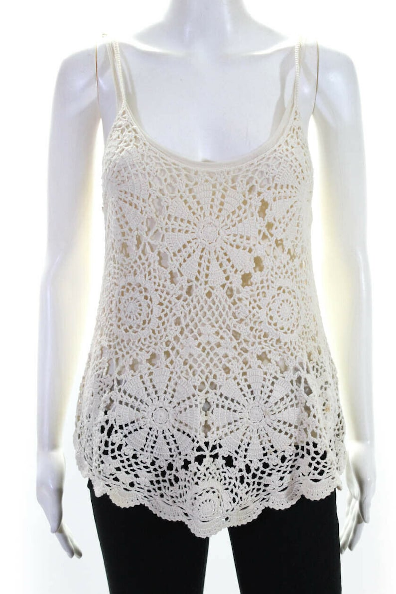 May include: A white crochet tank top with a scalloped hem. The top is made of a delicate, open-weave fabric with a floral pattern.
