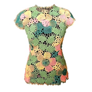 May include: A crocheted top with a floral design in shades of green, yellow, pink, and peach. The top has short sleeves and a round neckline.
