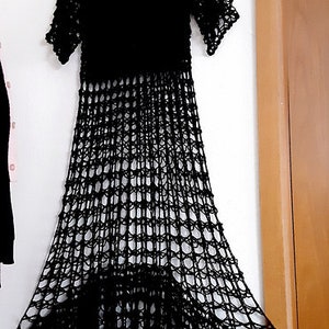 Puede incluir: Un vestido de crochet negro con una silueta suelta y fluida. El vestido tiene un escote redondo y mangas cortas. La tela es un crochet delicado y de tejido abierto que crea un efecto transparente.