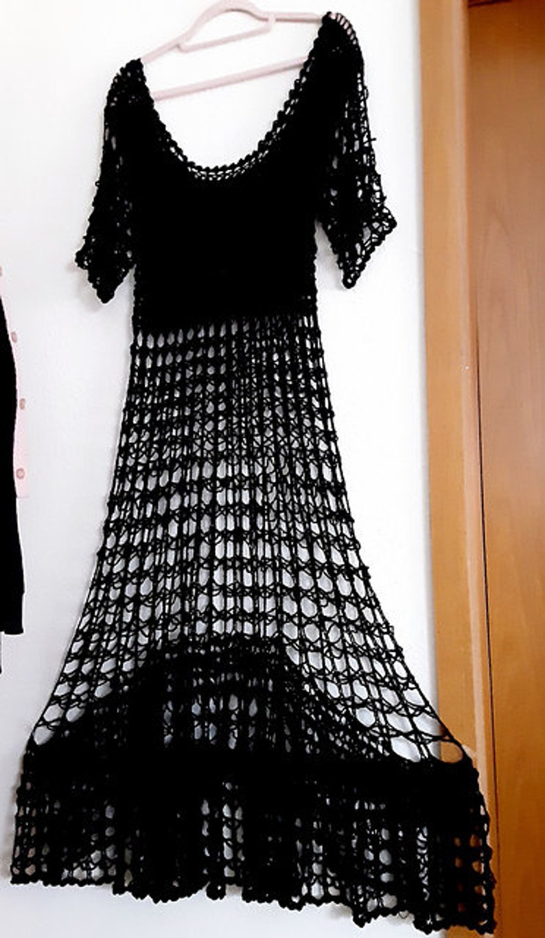 Puede incluir: Un vestido de crochet negro con una silueta suelta y fluida. El vestido tiene un escote redondo y mangas cortas. La tela es un crochet delicado y de tejido abierto que crea un efecto transparente.