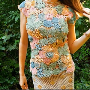May include: A crocheted top with a floral design in shades of pink, blue, and green. The top has a round neckline and short sleeves.