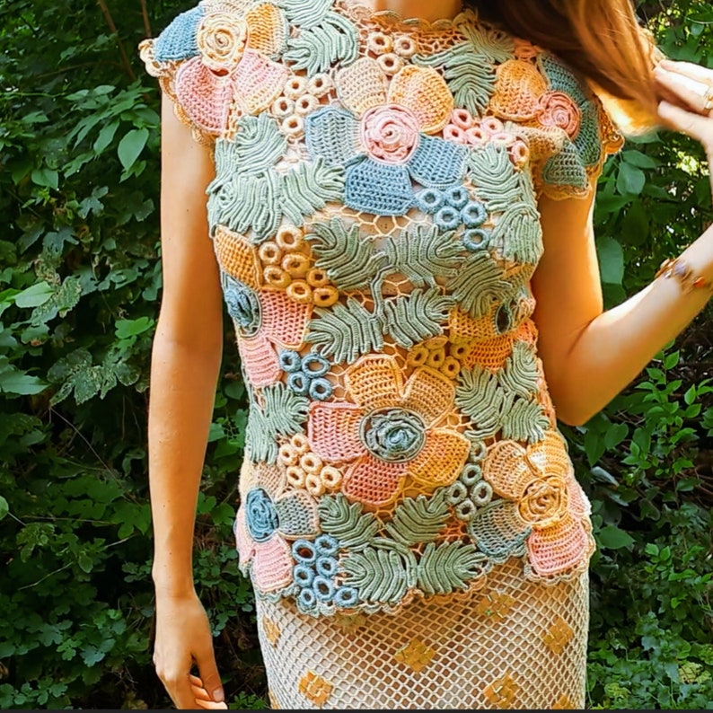 May include: A crocheted top with a floral design in shades of pink, blue, and green. The top has a round neckline and short sleeves.