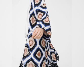 May include: A white crochet cardigan with a geometric pattern in shades of blue, black, and brown. The cardigan has a fringe trim.