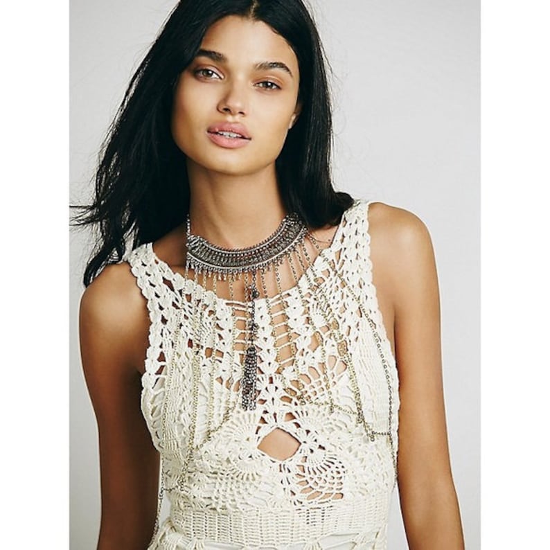 May include: A white crochet top with a silver chain necklace featuring a large pendant with multiple strands of chains and tassels.