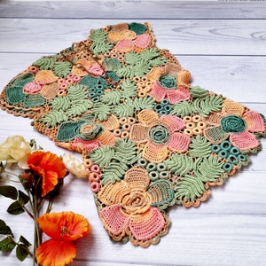 May include: A crocheted doily with a floral design in shades of green, pink, and orange. The doily is made with delicate stitches and features intricate details.